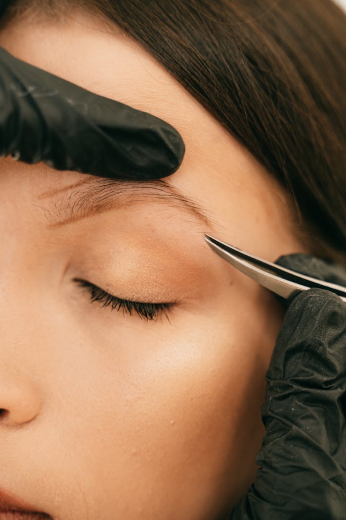pexels-photo-5178009 A detailed close-up of a woman having her eyebrow shaped with tweezers, highlighting professional beauty care.