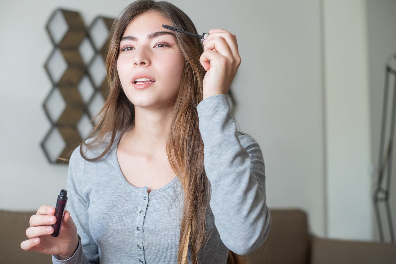 A young woman applying eyebrow makeup with a brush indoors.